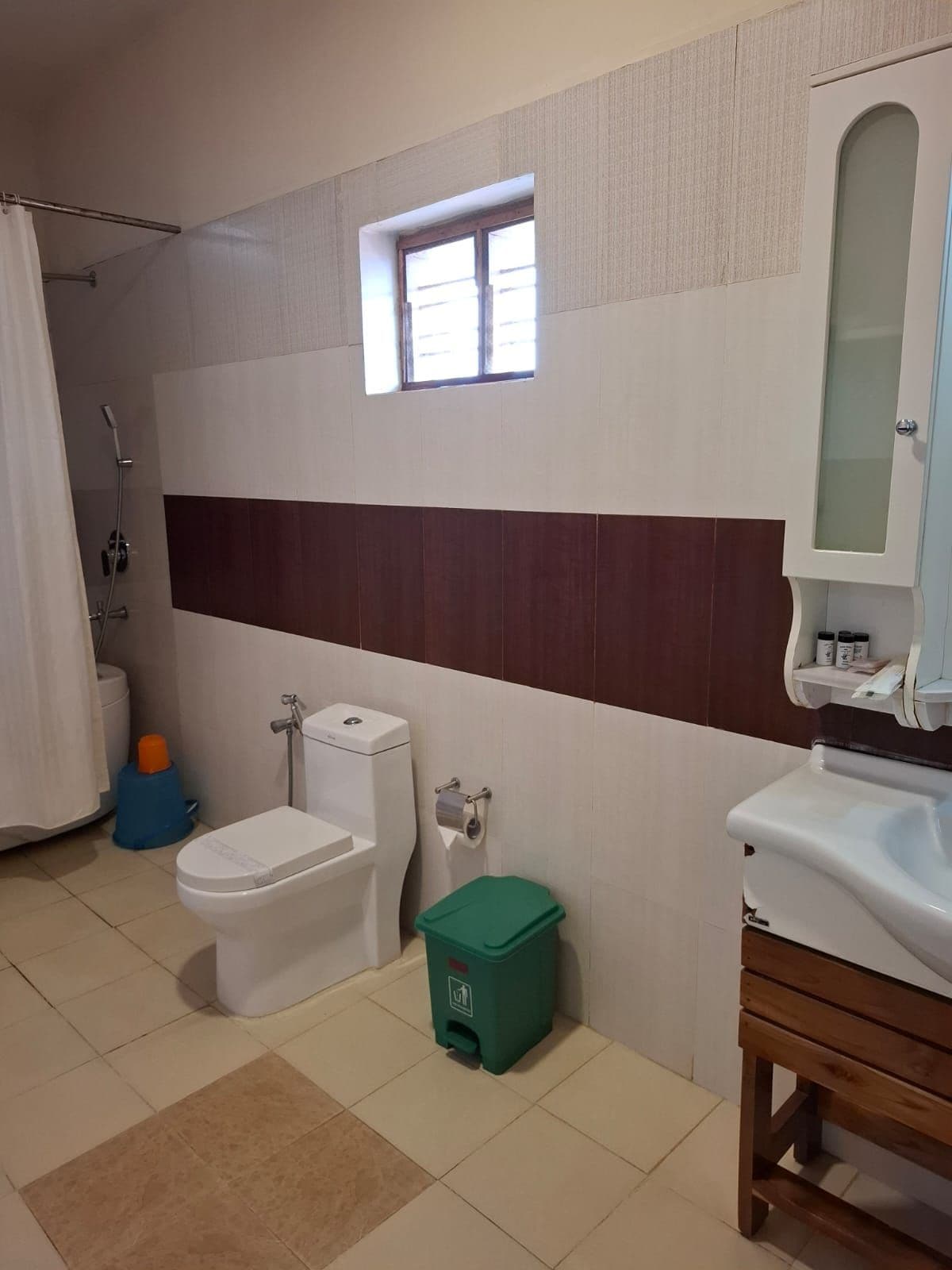 A bathroom with a toilet, bidet, shower, and a small window.