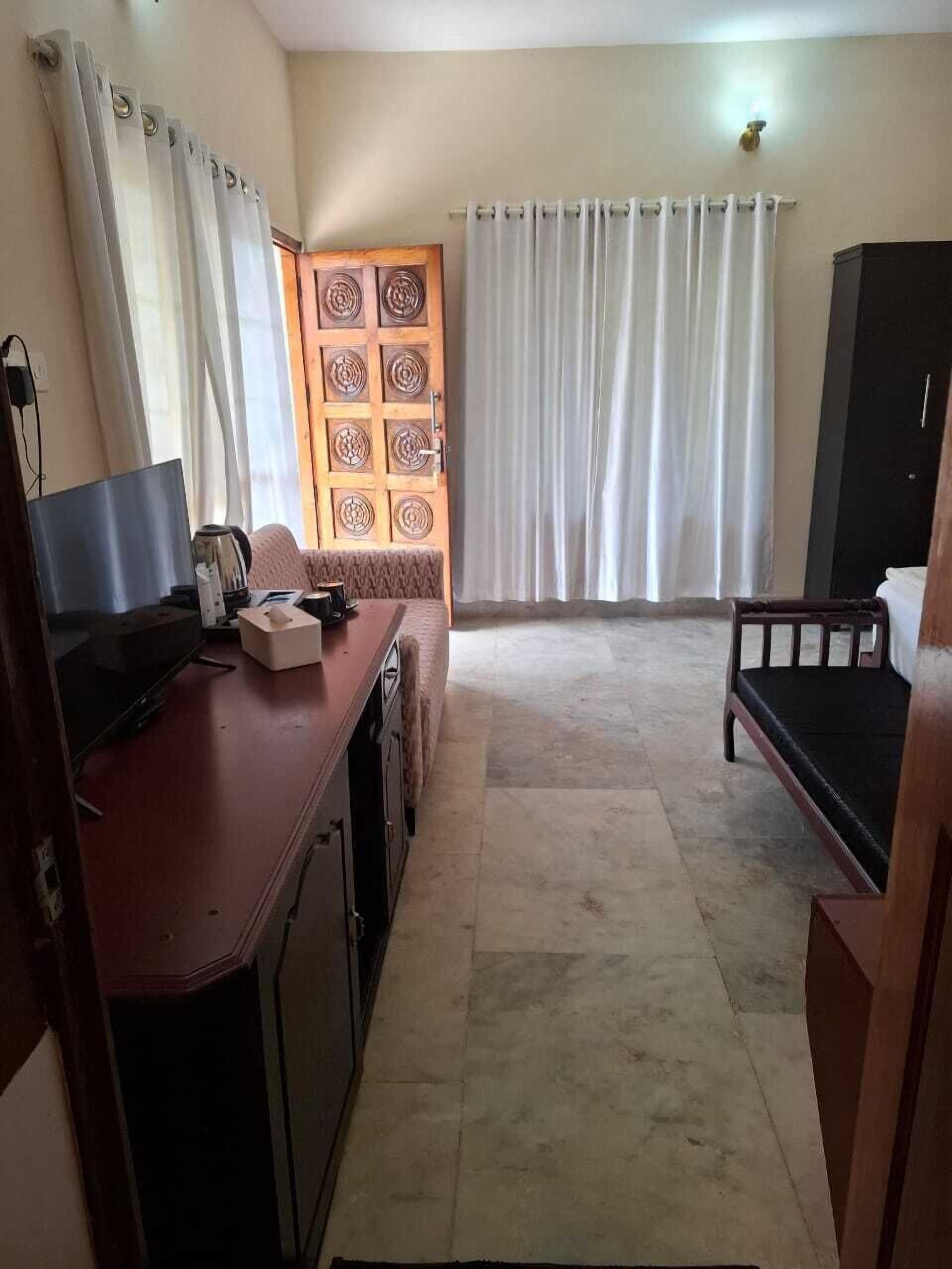 Una habitación con escritorio, televisor, sofá, armario y puerta con un panel decorativo.