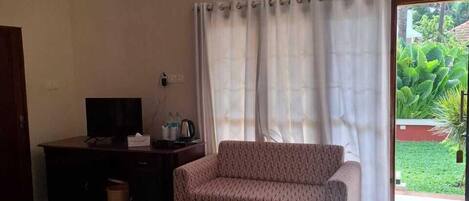A room with a bed, a sofa, a desk with a television, and a window with curtains.