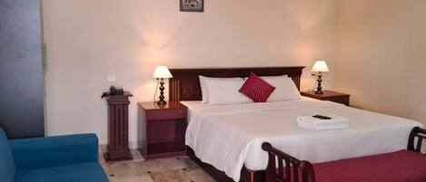 A hotel room with a bed, bedside lamps, a blue armchair, a marble floor, and an air conditioning unit.