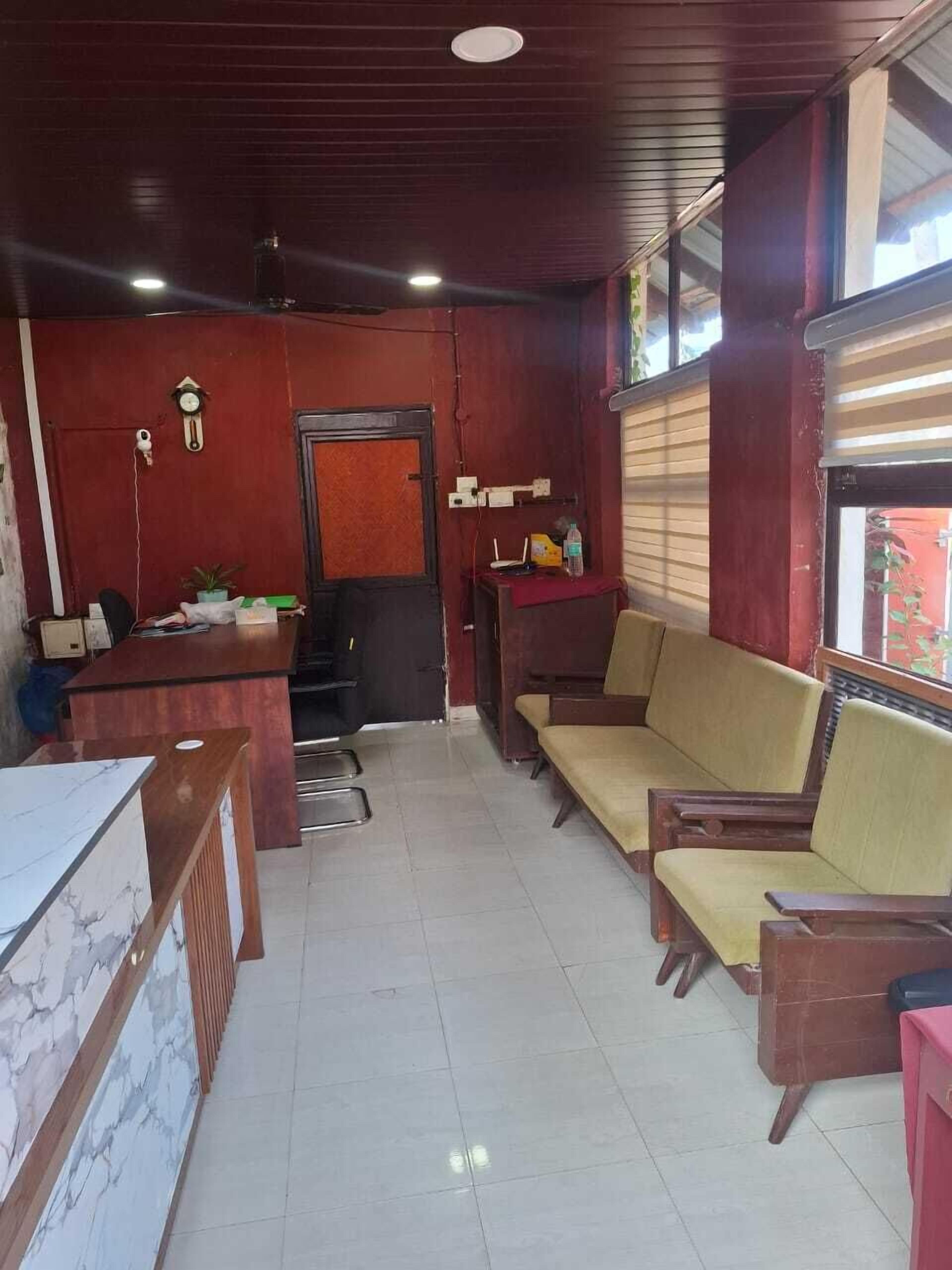 A room with a reception desk, a sofa, a chair, and a small table with a plant.