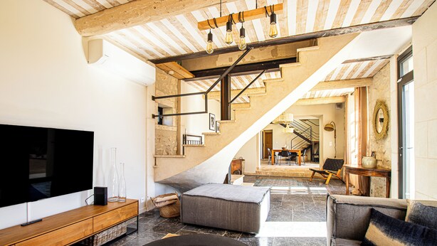Un salon moderne doté d’un grand téléviseur à écran plat, d’un meuble de rangement en bois, d’un canapé gris et d’un escalier menant à un niveau supérieur.
