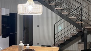 Une cuisine moderne avec une table en bois, un luminaire suspendu et un escalier doté d’une rampe en métal.