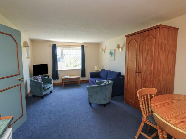 A room with a blue carpet, a wooden door, a blue sofa, a wooden table, and a wooden cabinet. - Moorhen (Newton Abbot)