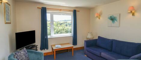 A living room with a TV, two sofas, a small table, and a window with curtains.