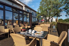 An outdoor dining area with wicker furniture and a table set for a meal. - Oakwood (Newton Abbot)