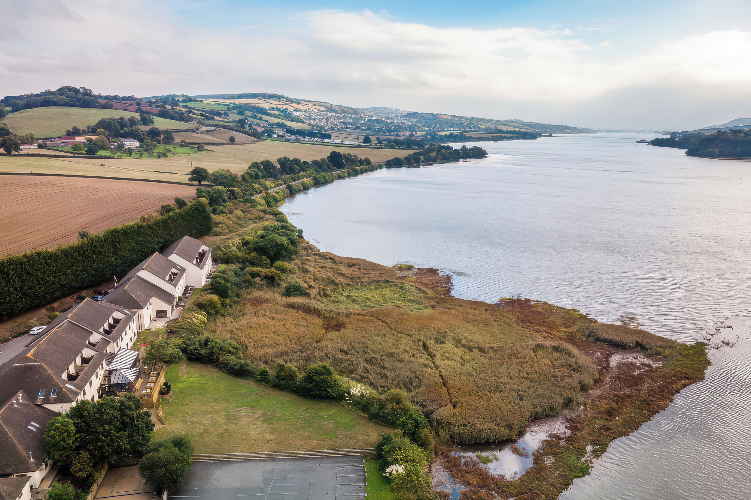 A riverside view with buildings, fields, and a distant town.