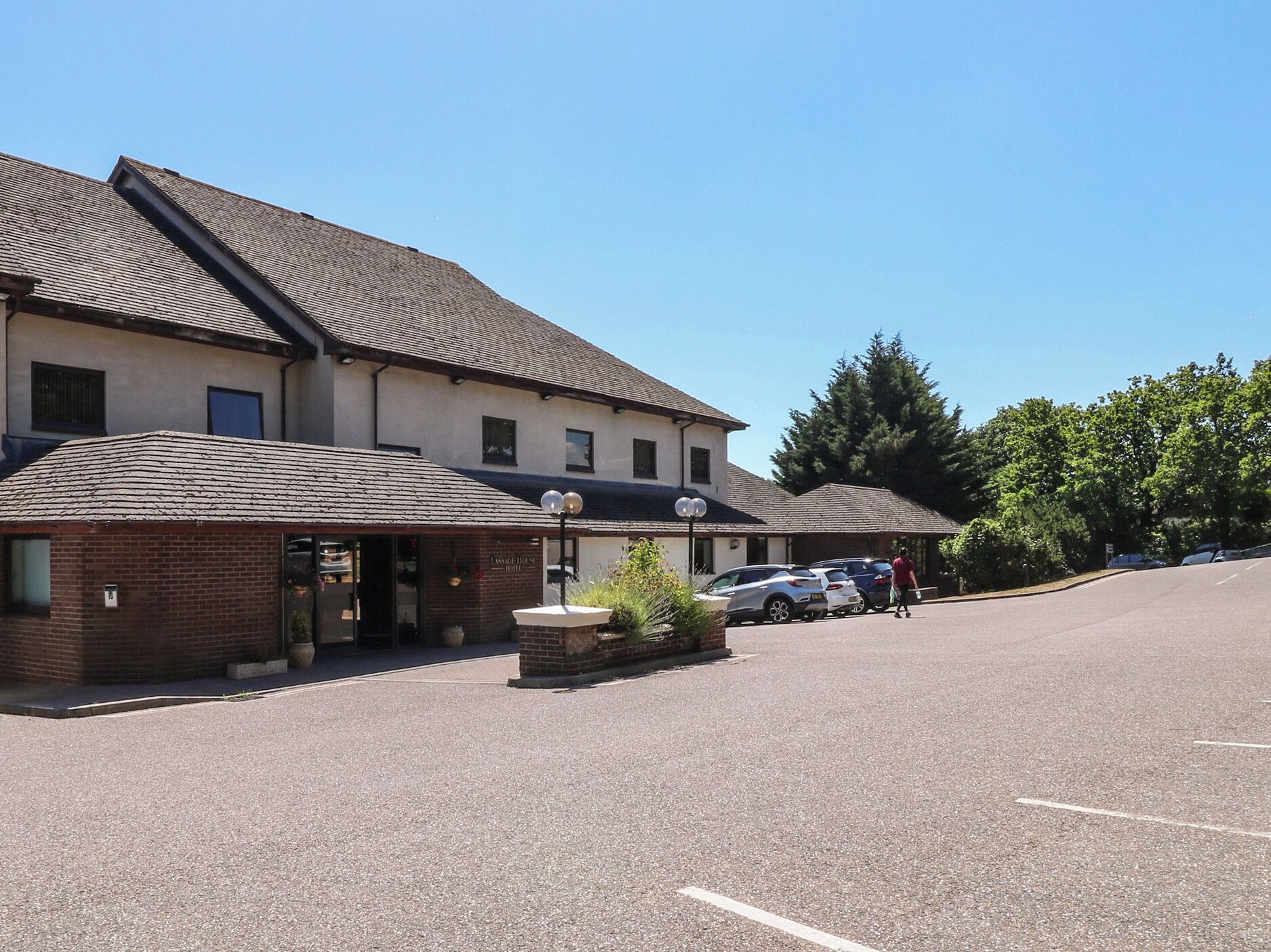 A building with a brick facade and a tiled roof, a parking lot, and a few parked cars.