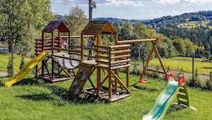 Een speeltuin met een houten klimconstructie, een glijbaan en een schommel.