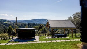 A gazebo with a metal roof, a circular outdoor heater, and a bench in a grassy area with a mountain view.
