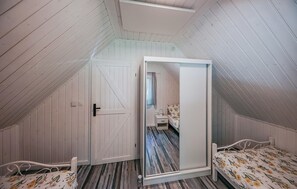 Une chambre avec un plafond en pente, un lit recouvert d’une literie à motifs floraux, une table de chevet et un miroir qui reflète la pièce.