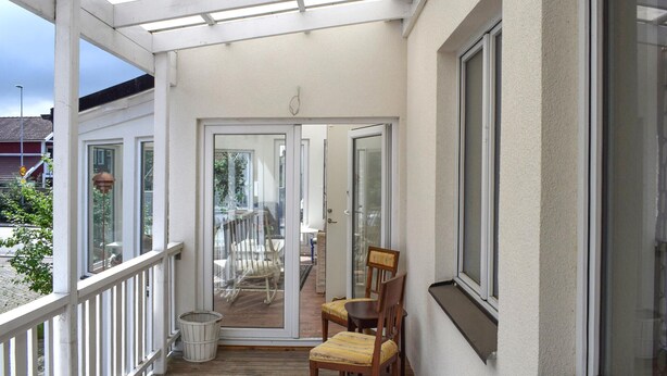 A covered balcony with a wooden floor, a white railing, and a glass door leading to an outdoor area with a table and chairs. - Lovely home in Höganäs with WiFi (Höganäs)