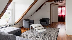 A modern loft bedroom with exposed wooden beams, a gray sofa, two armchairs, a white coffee table, and a patterned rug. - Lovely home in Höganäs with WiFi (Höganäs)