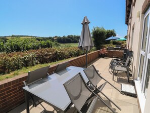 A patio with a table and chairs, a brick wall, and a view of a field. - Guillemot (Newton Abbot)