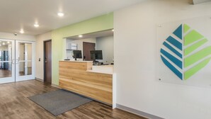 Un área de recepción con un mostrador de madera, una pared de acento verde y un logotipo en la pared.