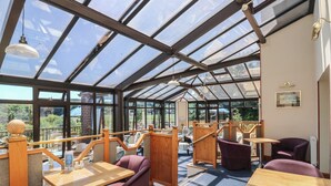 A conservatory with wooden furniture, glass ceiling, and outdoor views. - Avocet (Newton Abbot)