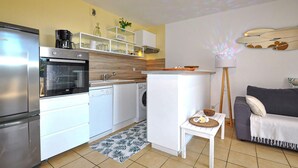 A compact kitchen with a refrigerator, oven, and dishwasher. There's a small table with a bowl and a lamp.