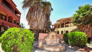 A courtyard with a fountain, palm trees, and a building with balconies.