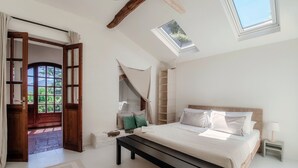 Une chambre avec un grand lit, une lucarne, une porte en bois et une vue sur la verdure.