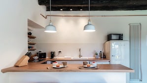 Une cuisine dotée d’un plan de travail en bois, de deux suspensions lumineuses, d’un four à micro-ondes et d’un réfrigérateur.