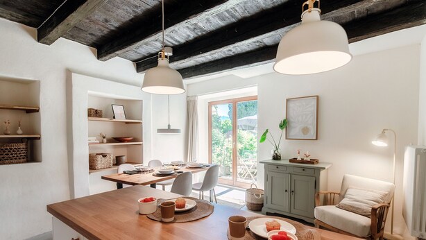 Une cuisine dotée de plans de travail en bois, une table à manger pour quatre personnes et une vue sur l’extérieur grâce à une grande fenêtre.