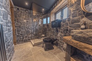 Une salle de bain aux murs en pierre, équipée de toilettes, d’une douche et d’un miroir.