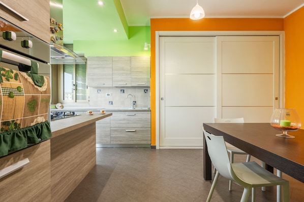 Une cuisine moderne avec un îlot central, un coin repas comprenant une table et des chaises, et un mur d’accent d’un orange vif.