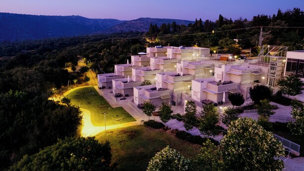 A modern hotel with multiple floors, outdoor seating areas, and a view of the surrounding hills.