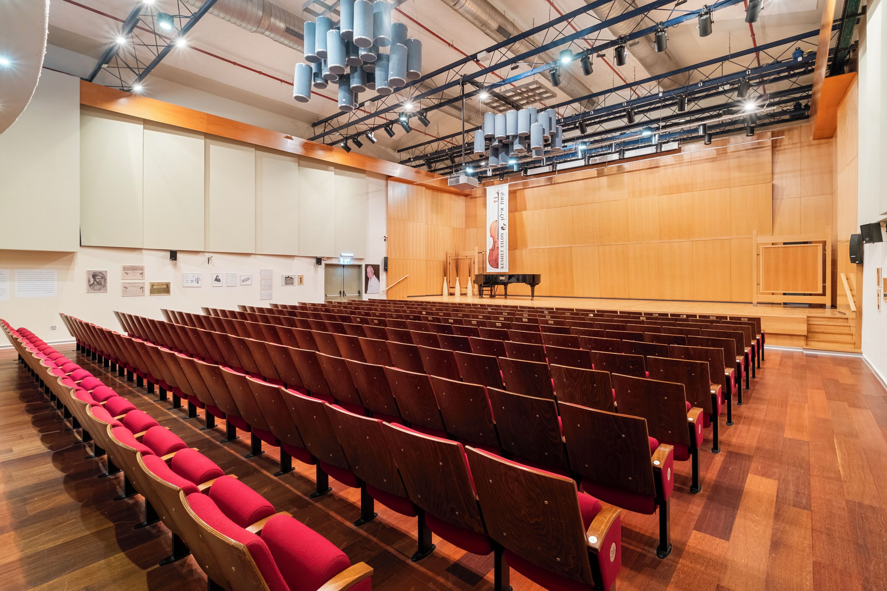 Un auditorium con file di sedie di legno e un palco con un pianoforte.
