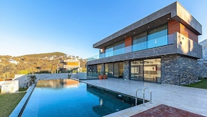 Une maison moderne à deux étages, dotée d’une piscine, de murs en pierre et offrant une vue sur le paysage environnant.