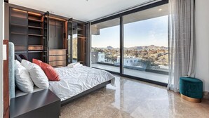 Une chambre moderne dotée d’un grand lit, d’une armoire intégrée et offrant une vue sur la ville grâce à de grandes fenêtres du sol au plafond.