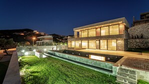 Une maison moderne à deux étages, dotée d’une façade en pierre, de grandes fenêtres et d’un espace extérieur bien éclairé avec une piscine.