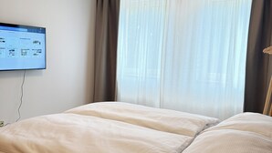 Une chambre d’hôtel avec un lit, un téléviseur à écran plat fixé au mur et une fenêtre avec des rideaux légers.