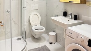 Une salle de bain moderne avec une douche à parois de verre, des toilettes, un lavabo et un lave-linge.