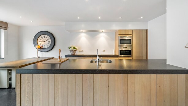 Una cocina moderna con una isla de madera, horno empotrado y un reloj en la pared.