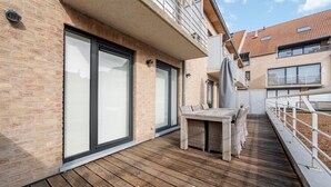 Una terraza de madera con una mesa y sillas, un muro de ladrillo y una puerta de cristal.