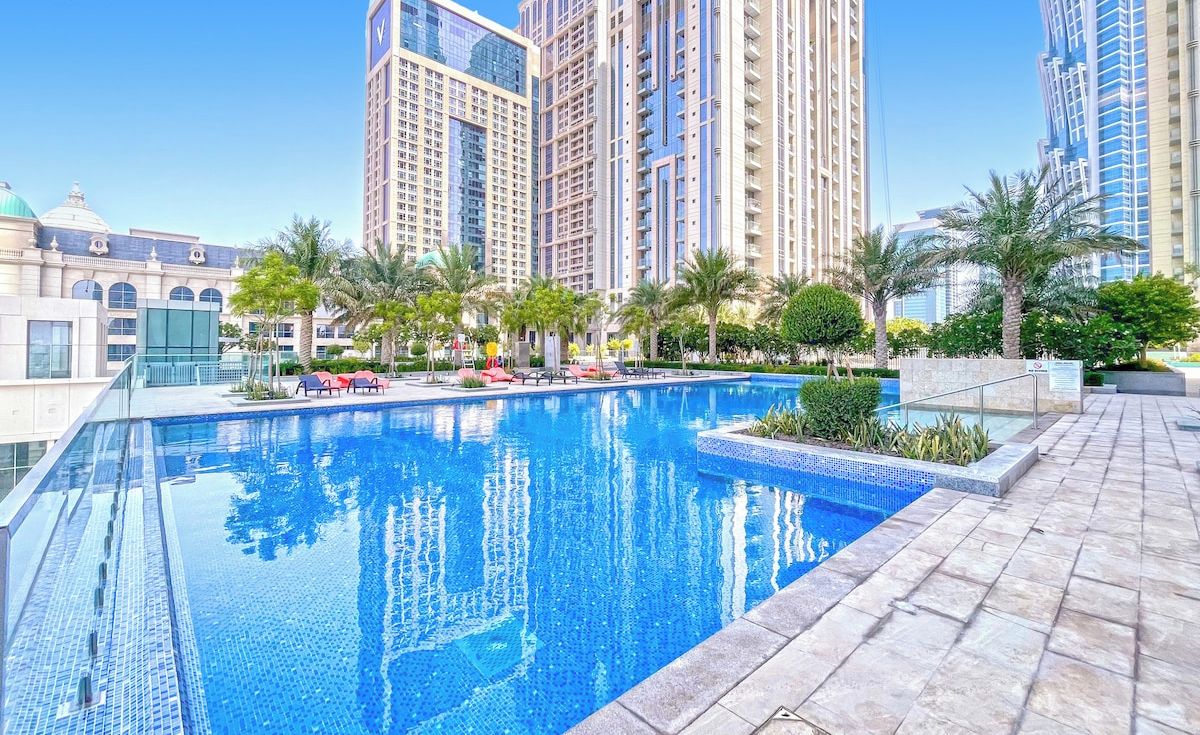A swimming pool with clear blue water, surrounded by palm trees and modern buildings.