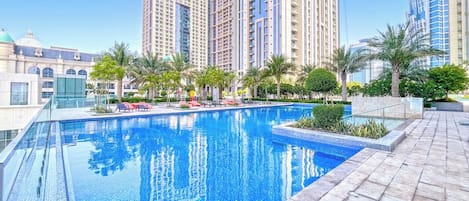 A swimming pool with clear blue water, surrounded by palm trees and modern buildings.