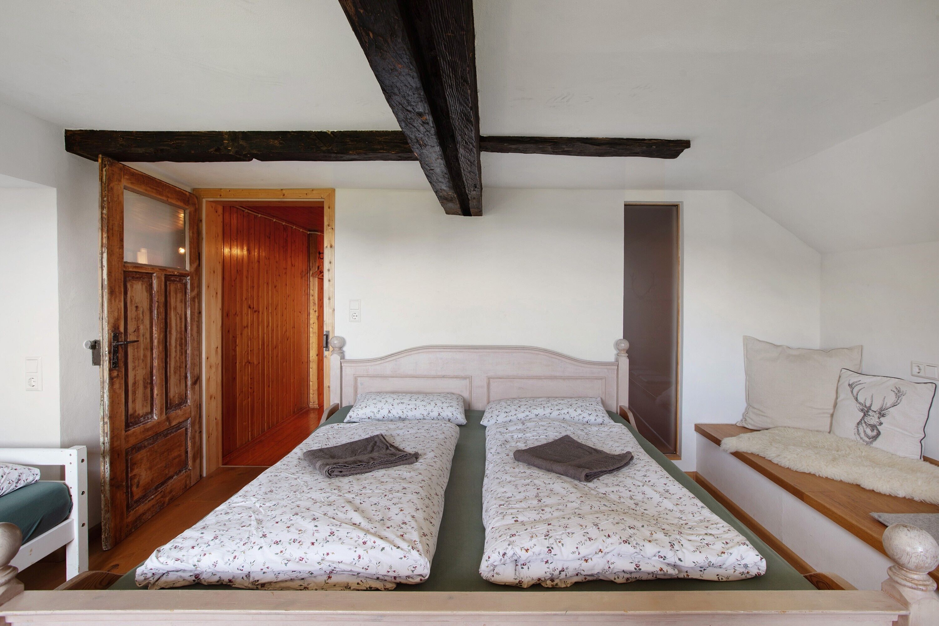 A room with two beds, a wooden door, a wooden beam ceiling, and a window.