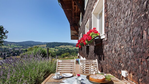 A wooden table set with plates, cups, and a plate of food, overlooking a scenic landscape.