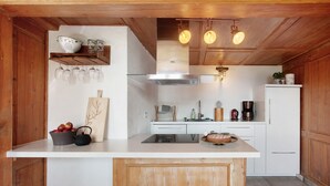 A kitchen with wooden cabinets, a white countertop, a central island, hanging wine glasses, and a coffee machine.