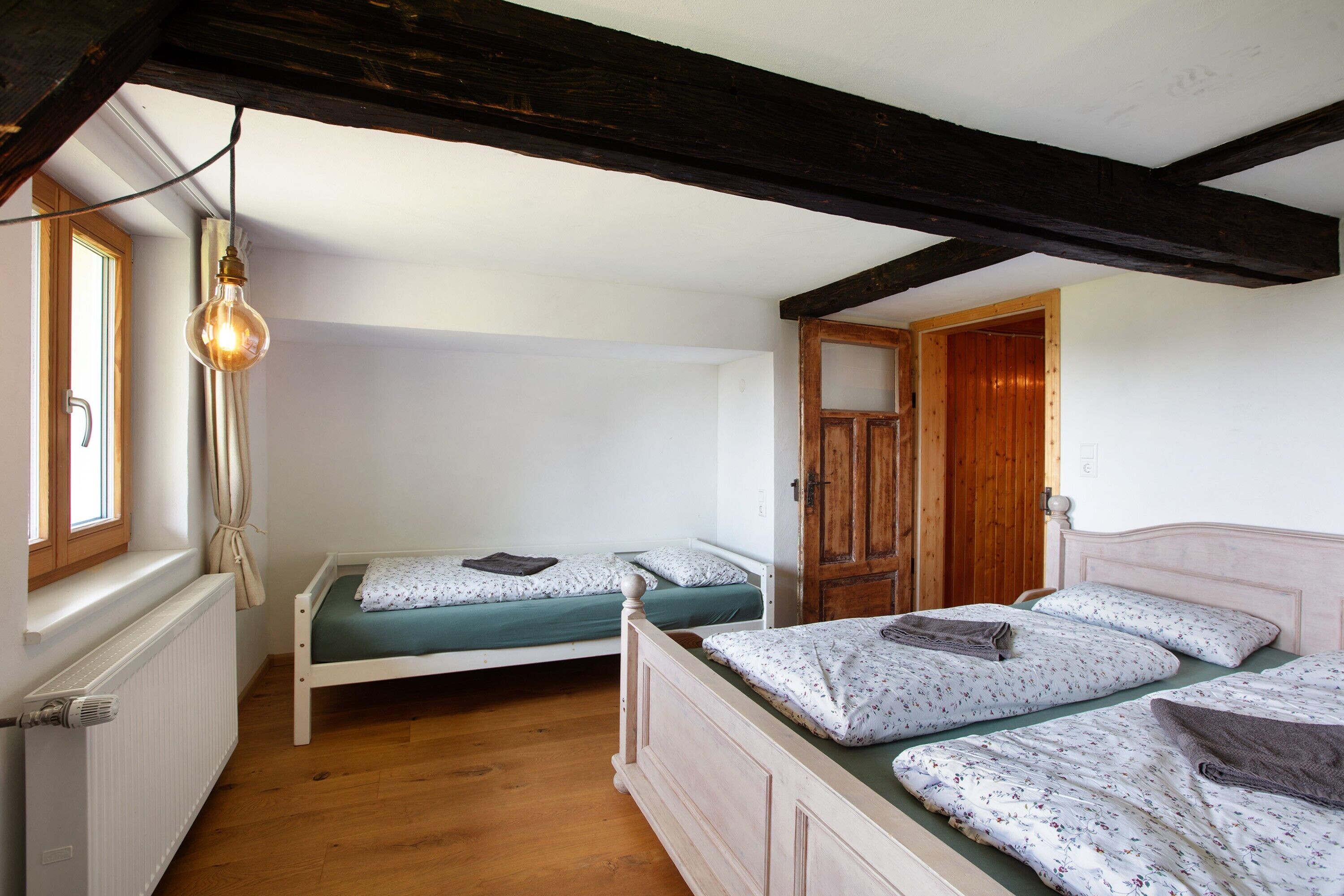 Een slaapkamer met twee eenpersoonsbedden, een houten deur, een radiator en een hanglamp.