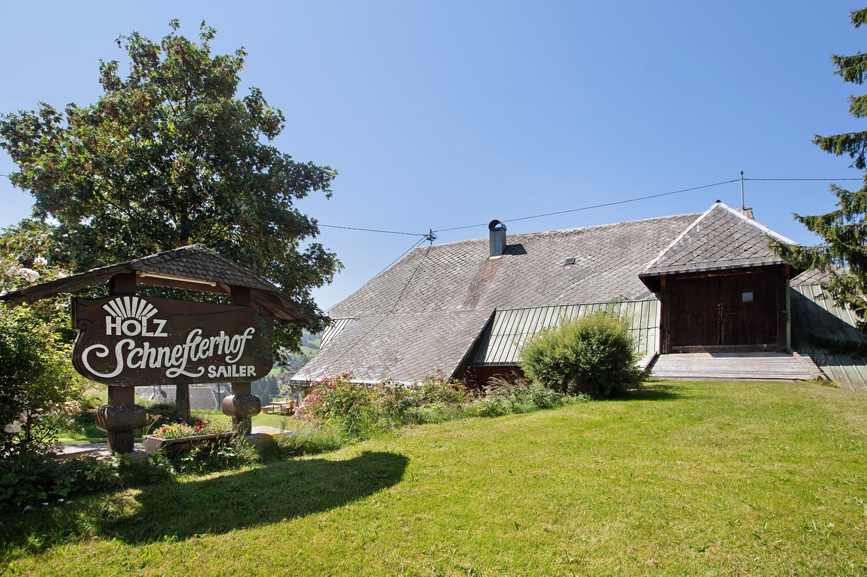 En traditionell träbyggnad med en skylt som visar texten: ”HOLZ Schneferhof Sailer”.