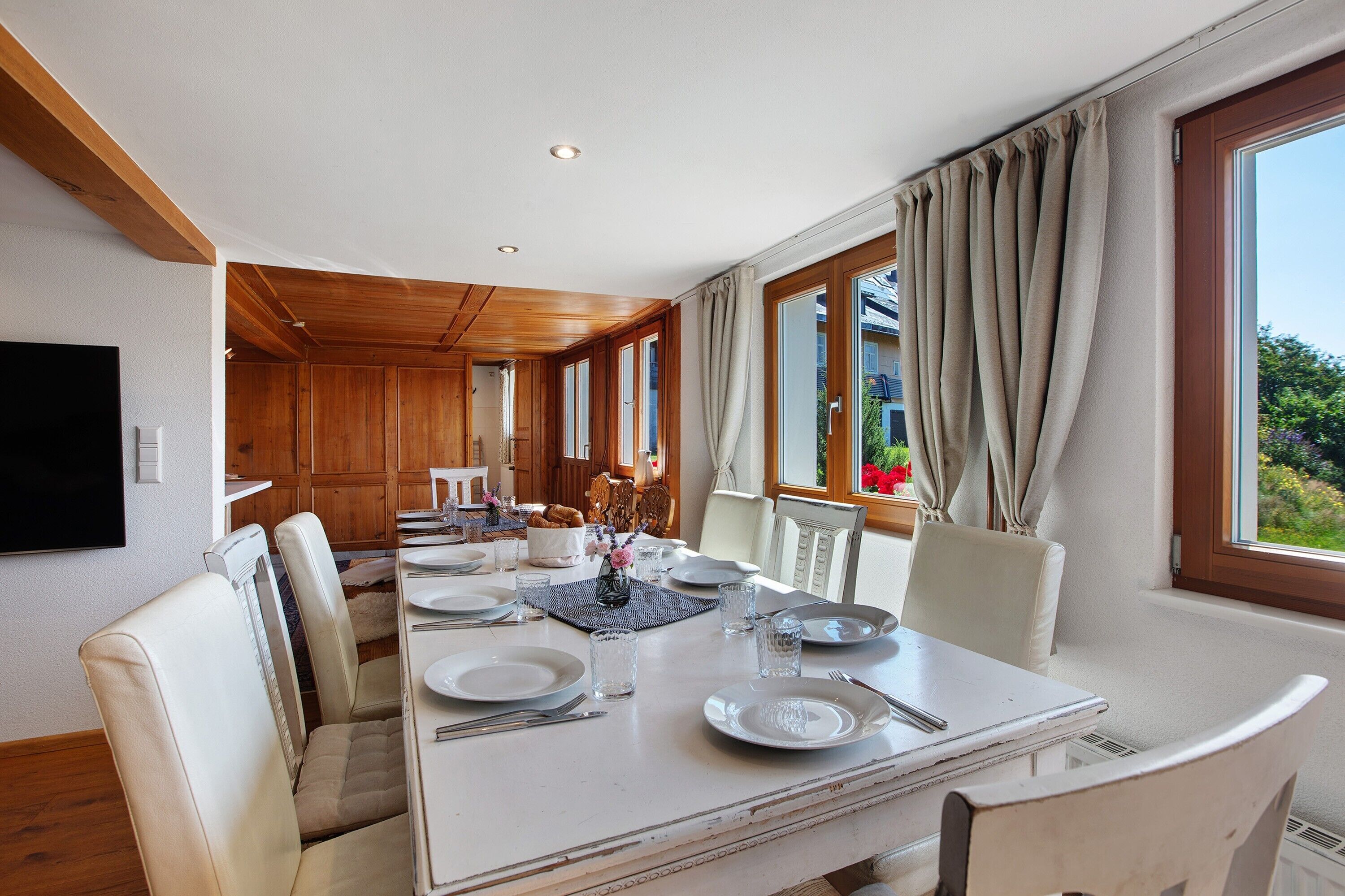 A dining area with a long table, chairs, and a television on the wall.