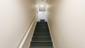 A narrow, carpeted stairway with white walls and a white handrail, leading to a door at the top. - Curwen Apartment (Workington)