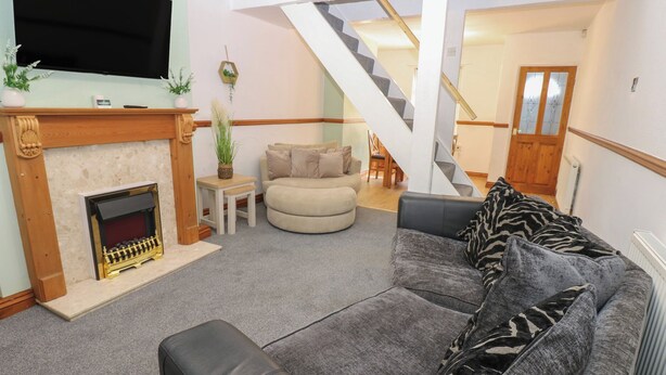 Ein Wohnzimmer mit Kamin, einer Couch, einem Fernseher und einer Treppe, die in einen anderen Raum führt.