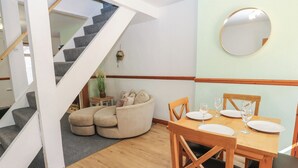 Ein Essbereich mit einem Holztisch, gedeckt für vier Personen, einer Treppe und einem beigefarbenen Sofa.