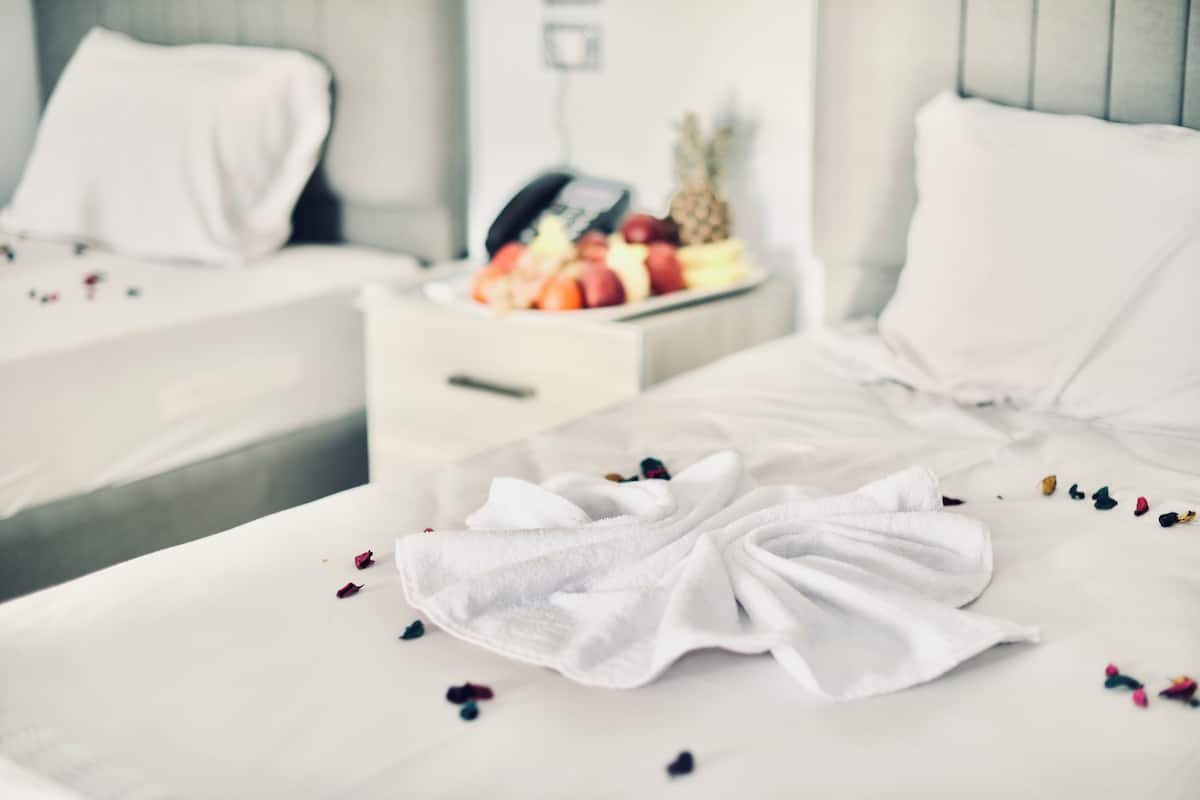 A hotel room with two beds, a bedside table with a fruit basket, and a white towel on one bed.