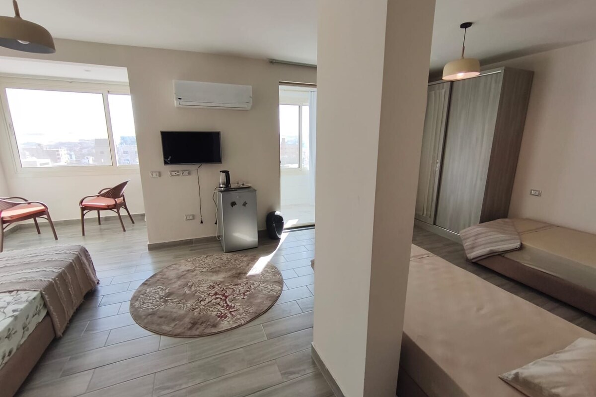 Un salon moderne avec un canapé, une table basse et un téléviseur. Une fenêtre offre une vue sur les bâtiments.
