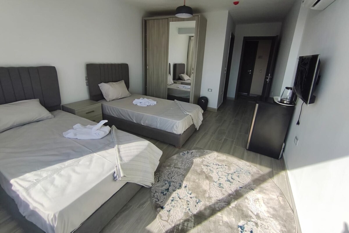 Una habitación de hotel moderna con dos camas, un televisor de pantalla plana, una cafetera y un espejo.